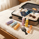 photo professionnelle  ensemble de produits capillaires pour cheveux crépus beauté insolente disposés sur un lit a côté d'une valise moderne ouverte avec des vêtements d'été pliés, passeport, lunettes. 