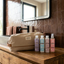 photo professionnelle lifestyle,  ensemble de 4 produits capillaires beauté insolente pour cheveux ondulés présenté sur un meuble a côté d'un sac  beige dans une salle de bain moderne. 