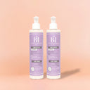 Photo publicitaire qualité studio, un lot de 2 flacons créme boucle beauté insolente présentés debout aligner droit et identique sur un fond neutre couleur pêche claire.