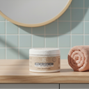 photo professionnelle, scène lifestyle, pot de crème pure énergie beauté insolente posé dans une salle de bain moderne, tons pastels et bois clair, serviette rose pêche roulée et posée à côté.